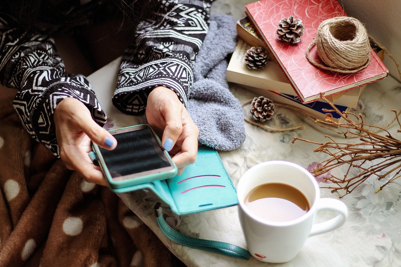 Une jeune femme a un téléphone dans la main, un café sur la table.